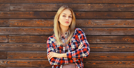 Portrait of beautiful confident caucasian blonde young woman with crossed arms in casual checkered shirt in the city - obrazy, fototapety, plakaty