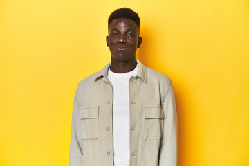 Stylish young African man on vibrant yellow studio background, blows cheeks, has tired expression....