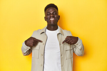 Stylish young African man on vibrant yellow studio background, surprised pointing with finger, smiling broadly.
