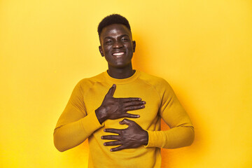 Stylish young African man on vibrant yellow studio background, laughs happily and has fun keeping...