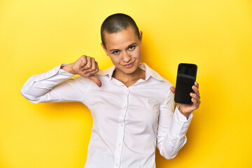 Shaved head woman holding mobile, yellow background feels proud and self confident, example to follow.