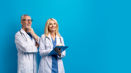 Cheerful senior doctors looking at copy space, blue background