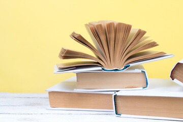 Open books, hardback colorful books on wooden table. yellow background. Back to school. Copy space for text. Education business concept.