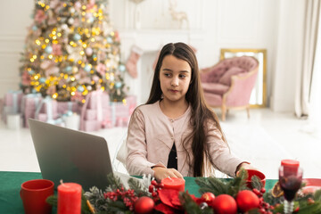 teenage girl works at home remotely with laptop on the background of a Christmas tree. Quarantine, work on holidays. atmosphere and work at home