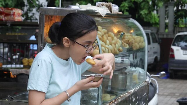 Happy Indian woman having North Indian subcontinent popular street food. Hand cracking panipuri. Street food. Appetizer.