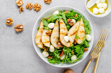 Grilled Pear Salad, Salad with Pear, Arugula, Mozzarella Pearls, Walnuts and Dressing over Bright Background