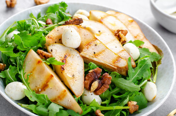 Grilled Pear Salad, Salad with Pear, Arugula, Mozzarella Pearls, Walnuts and Dressing over Bright Background