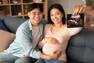 Joyful japanese couple showing sonogram photo of their baby indoor