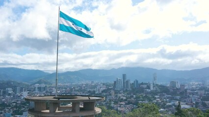 Aerial circling over the flag of Honduras and with a parallax effect with Tegucigalpa City as background 