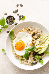 Savory oatmeal with fried sunny side up egg, avocado and pumpkin seeds for healthy breakfast