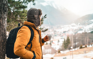 Young hiker taking a break while enjoying hot tea in the mountains. Backpacker wearing winter clothes spending his time alone in the forest.