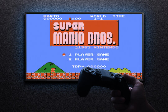 Super Mario Bros classic video game on TV with gamepad in hand on black textured wall with blue light. Retro game emulator for pc concept. Astana, Kazakhstan - August 31, 2023.