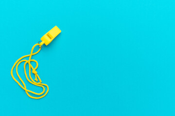 Plastic referee whistle on turquoise blue background with copy space. Flat lay image of yellow referee whistle.
