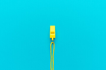 Plastic referee whistle on turquoise blue background with copy space. Flat lay image of yellow...