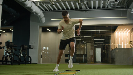 Professional footballer man with muscular legs run in gym use sport equipment ladder warm up cardio...