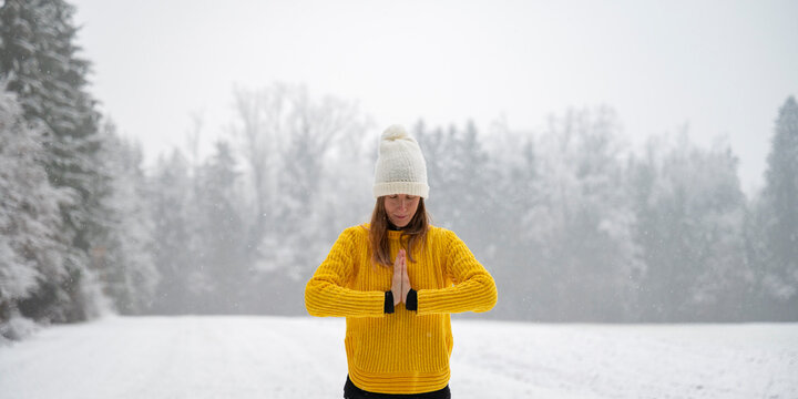 Peaceful young woman meditating or praying in winter nature with her palms joined in front of her chest