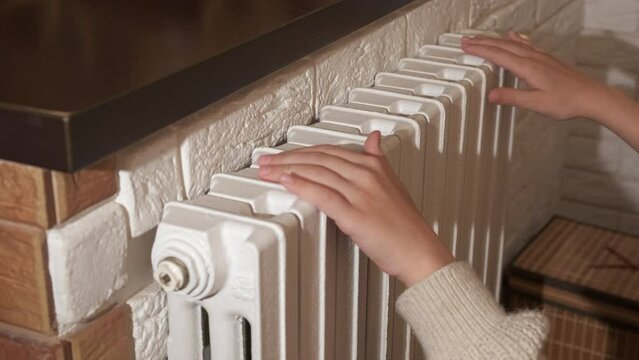 Putting hands on central radiator. A child put her hands on radiator to get warm at home. A concept of home heating crisis.