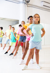 Focused positive tween girl with group of children standing in row one by one, learning classical...
