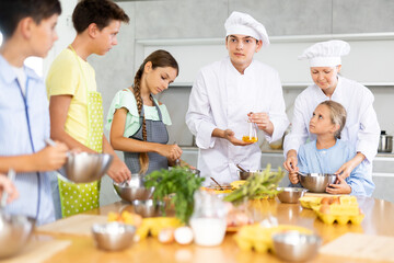 ..Young guy and adult woman chef at master class teaches group of children how to cook food
