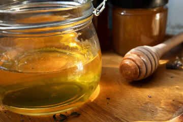 fresh natural  linden honey in big glass jar  at wooden tray with wooden  honey spoon aound herb...