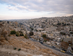 Cityscape of Amman, as seen from the Amman Citadel. Houses are built over the sloping hillside, in the center of which is the ruin of the enormous Roman Theatre, showing a mix of old and new elements.