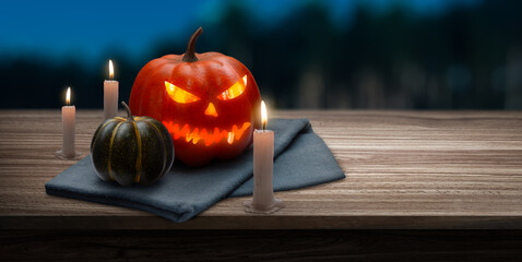 Jack O' Lantern with glowing eyes on a wooden table next to some candles on a spooky Halloween night