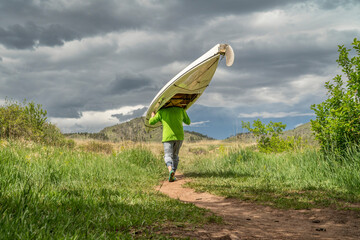 senior male is portaging a decked expedition canoe at foothills of northern Colorado in spring...