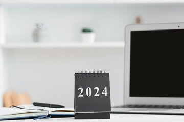 Calendar with figure 2024 and laptop on table in room