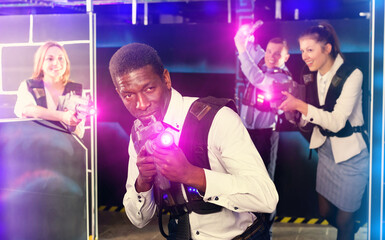 Fototapeta na wymiar African American man in business suit holding a his laser gun and playing laser tag with his associates