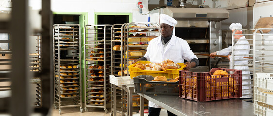 Positive african-american bakery worker lays fresh bread. High quality photo