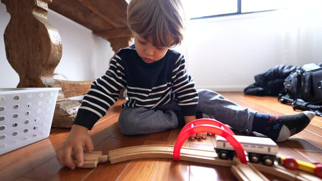 Child plays with retro toys on hardwood floor. One small boy playing indoors with train wooden tracks by himself