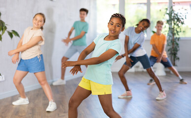 Positive juvenile girl engaged in Breakdancing together with children's group in training room during workout session