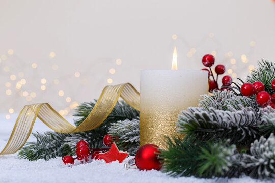 Christmas or new year candle with festive ornaments and bokeh lights on snow, family holidays