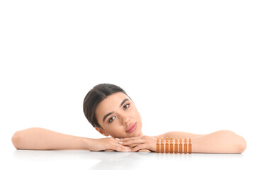 Beautiful young woman with ampules on table against white background