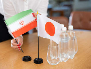 Little flag of Japan on table with bottles of water and flag of Iran put next to it by positive...