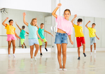 Obraz premium Portrait of cheerful preteen girl learning energetic dance moves with group of children in choreography class .
