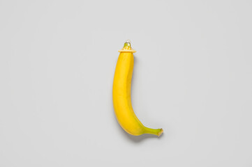Fresh banana with condom on grey background. Sex education concept