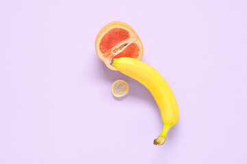 Fresh banana with grapefruit and condom on purple background. Sex education concept