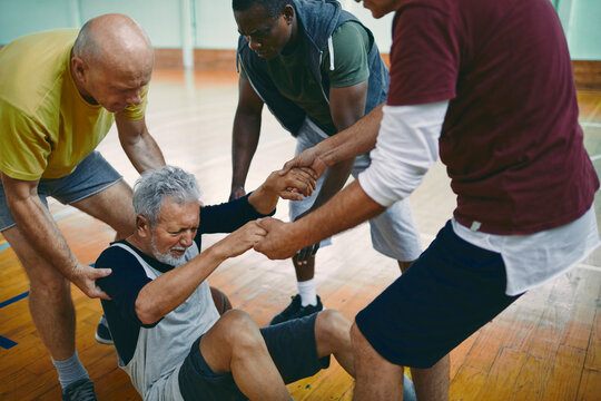 Senior man getting injured playing basketball with his friends in an indoor basketball gym