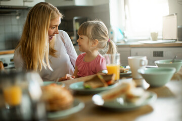 Young Caucasian mother having breakfast with her daughter in the kitchen
