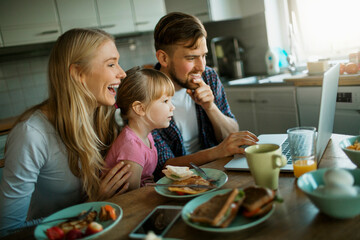 Young family having breakfast and using a laptop in the kitchen at home