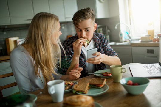 Young Caucasian couple using a smartphone while having breakfast in the kitchen