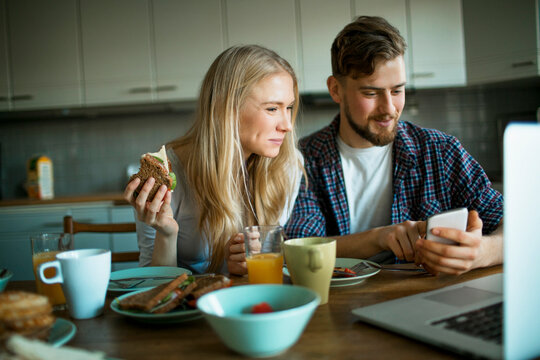 Young Caucasian couple using a smartphone while having breakfast in the kitchen