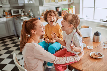 Young mother and her kids having breakfast together and being messy in the kitchen