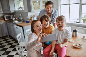 Young family taking a selfie on a smartphone while having breakfast and being messy in the kitchen