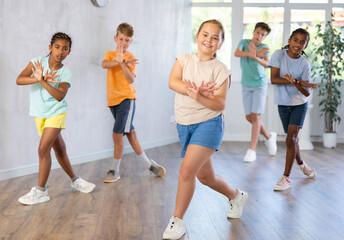 Active preteen girl practicing sport dances with other children in training hall during dancing...