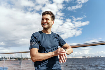 A runner smiles happily, a man uses a smartwatch for sports. A strong young trainer doing running exercises.  A confident person in fitness clothes and sneakers.