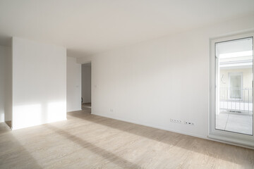 Unfurnished living room in new apartment. Sunlight enters the room and hits the wooden floor. Walls...