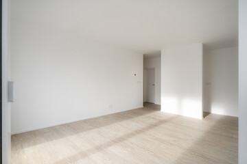 Empty unfurnished living room in a new apartment. Sunlight enters the room and hits the wooden...