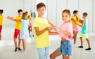 Portrait of positive tweenagers practicing slow ballroom dances in pairs in choreographic studio.